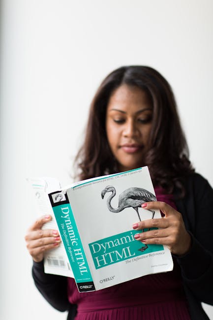 The image shows a woman with medium-length dark hair and light skin reading a book titled 'Dynamic HTML' by O'Reilly, which features an illustration of a flamingo on the cover. She is wearing a black